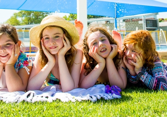 Image of four children lying on beach towels at the swimming pool